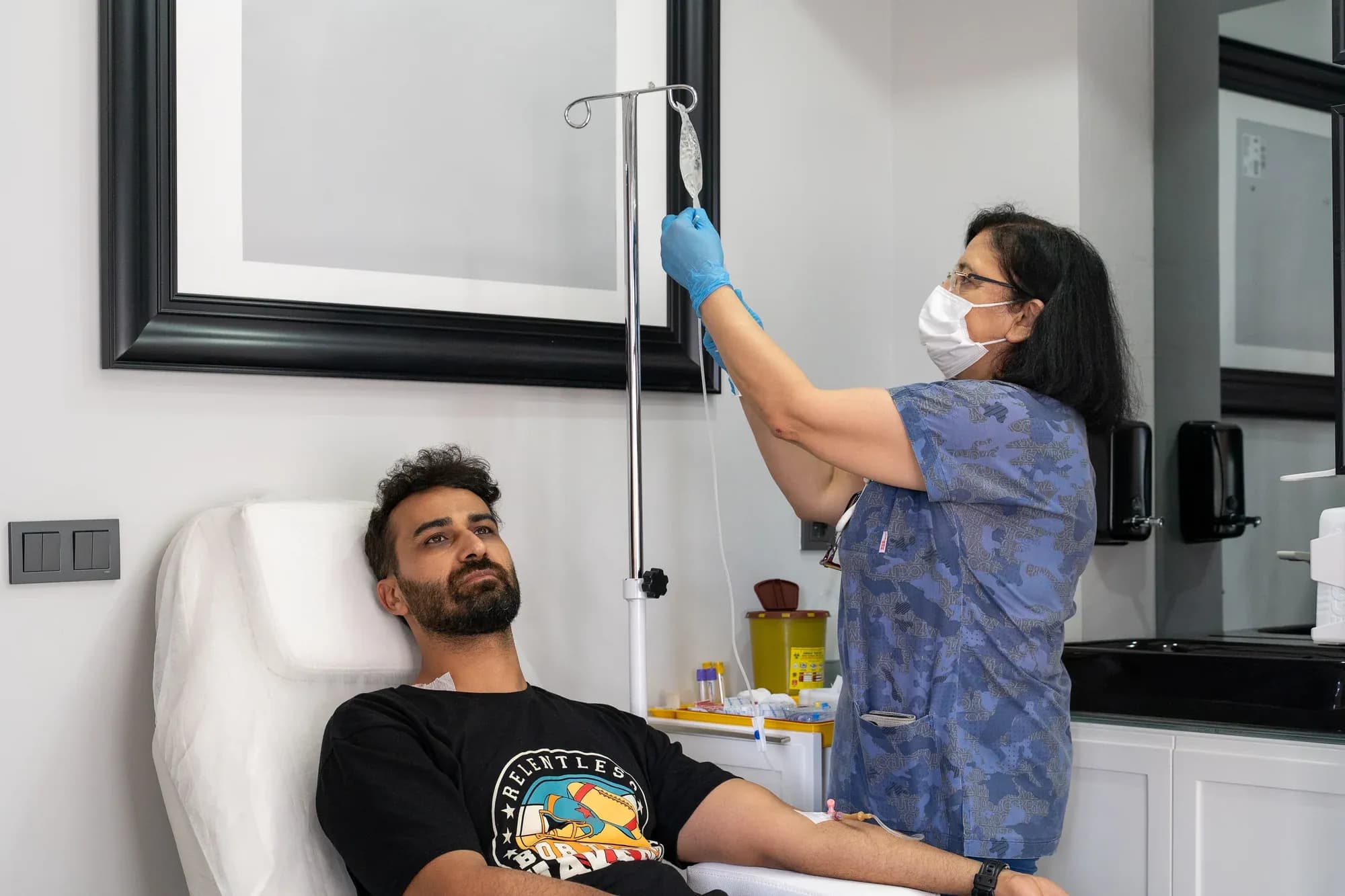 Klinik uygulama koltuğu yanında eldivenli sağlık çalışanı serum düzeneğini hazırlıyor.