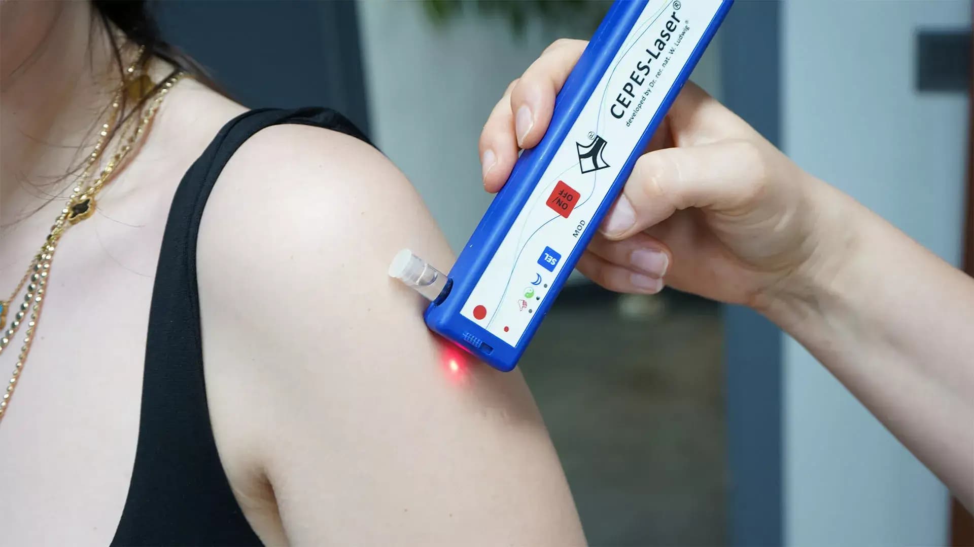 Mavi CEPES-Laser cihazı bir kişinin omuz bölgesine yöneltilmiş; cilt üzerinde kırmızı ışık görülüyor.