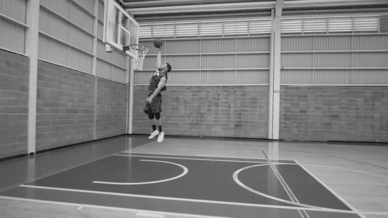 Schwarz-weiße Aufnahme eines Basketballspielers, der in einer Halle zum Korb springt.
