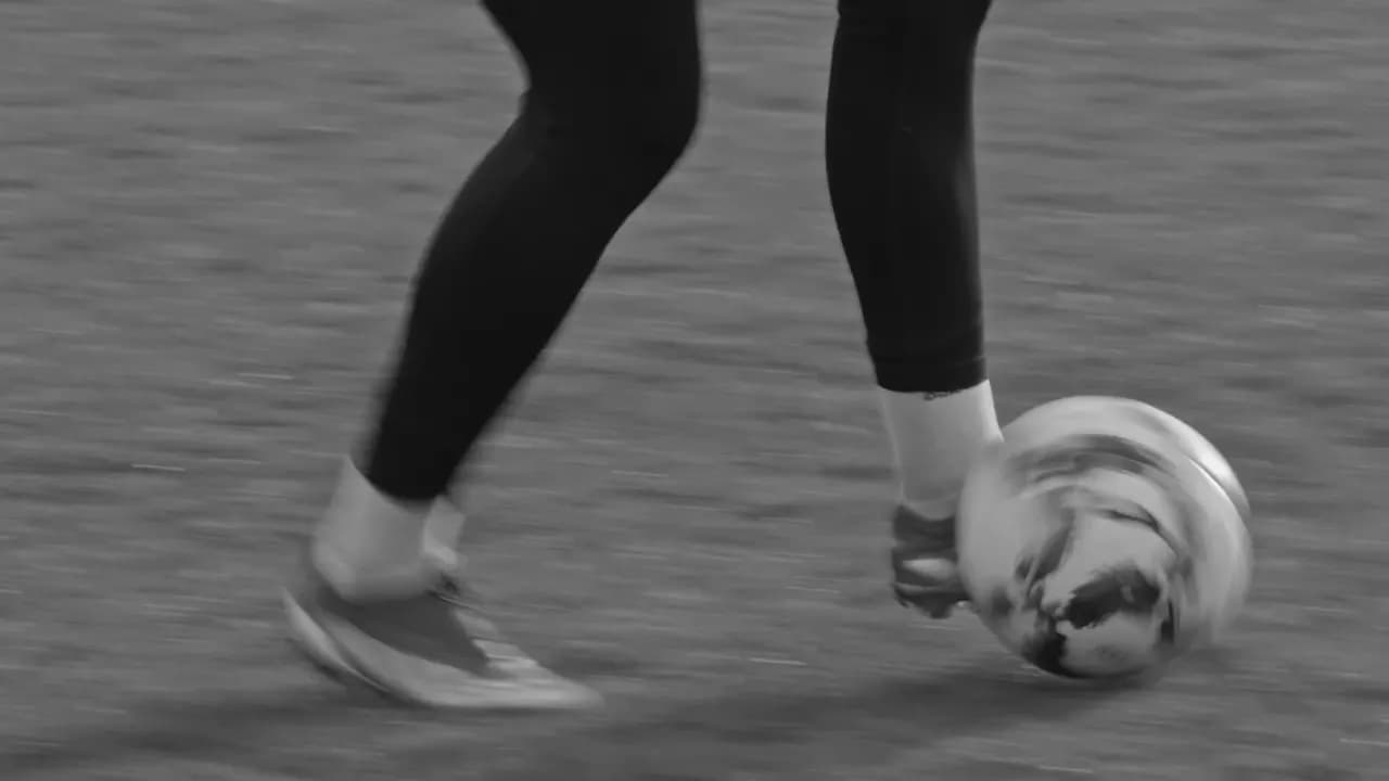 Schwarz-weiße Nahaufnahme der Beine und des Balls beim Dribbeln auf einem Rasenplatz.