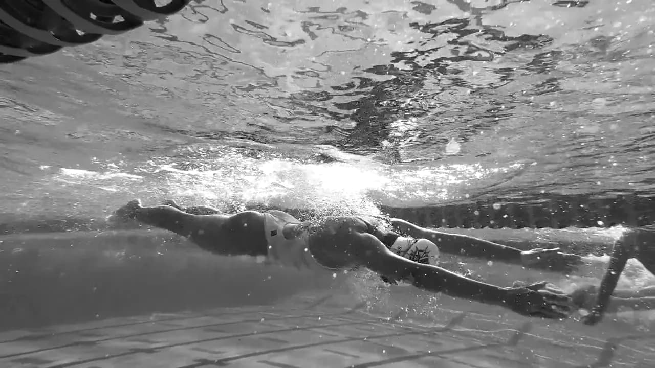 Schwarz-weiße Unterwasseraufnahme einer Person beim Freistilschwimmen im Schwimmbecken.